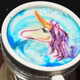 Overhead view of colorful unicorn portrait within latte foam in coffee cup on silver saucer